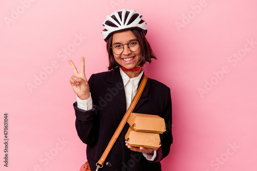 Young business mixed race woman wearing bike helmet holding burger isolated on pink background showing number two with fingers.