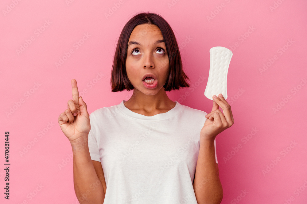 Young mixed race woman holding a compress isolated on pink background pointing upside with opened mouth. Young mixed race woman holding a compress isolated on pink background pointing upside with opened mouth.