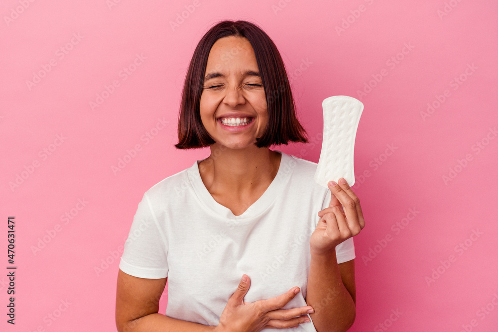 Young mixed race woman holding a compress isolated on pink background laughing and having fun. Young mixed race woman holding a compress isolated on pink background laughing and having fun.