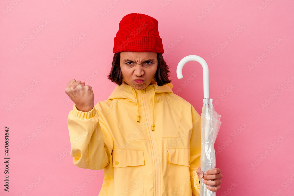 Young mixed race woman holding an umbrella isolated on pink background showing fist to camera, aggressive facial expression. Young mixed race woman holding an umbrella isolated on pink background showing fist to camera, aggressive facial expression.