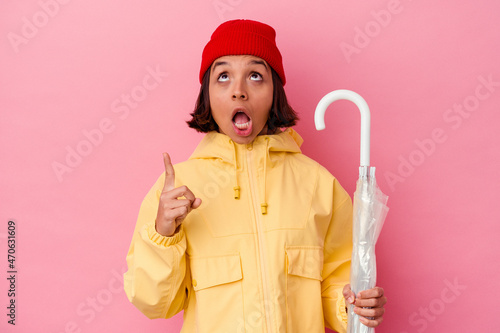 Young mixed race woman holding an umbrella isolated on pink background pointing upside with opened mouth.