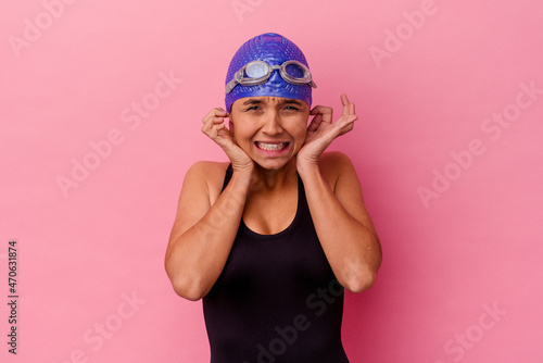 Young swimmer mixed race woman isolated on pink background covering ears with hands.