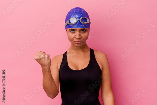 Young swimmer mixed race woman isolated on pink background showing fist to camera, aggressive facial expression.
