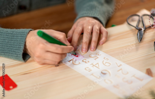 Fototapeta Naklejka Na Ścianę i Meble -  christmas, winter holidays and hobby concept - close up of hands with stencil drawing number one with green marker on tag and making advent calendar