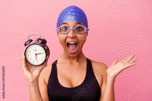 A confident swimmer with cap and goggles holds a trusty alarm clock. © Asier