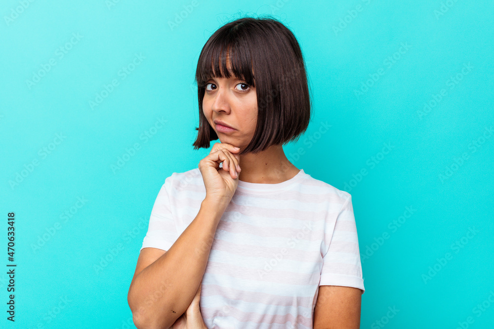 Young mixed race woman isolated on blue background suspicious, uncertain, examining you. Young mixed race woman isolated on blue background suspicious, uncertain, examining you.