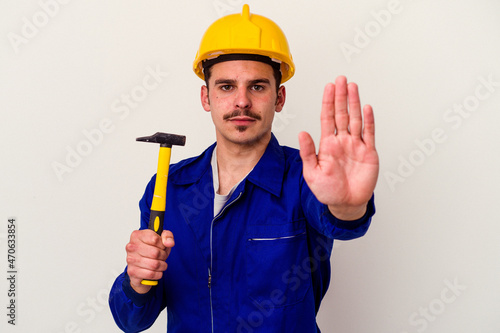 Young caucasian worker man holding a hammer isolated on white background standing with outstretched hand showing stop sign, preventing you.