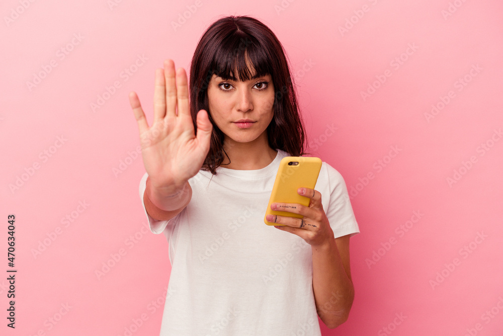 Young caucasian woman holding a mobile phone isolated on pink background standing with outstretched hand showing stop sign, preventing you. Young caucasian woman holding a mobile phone isolated on pink background standing with outstretched hand showing stop sign, preventing you.