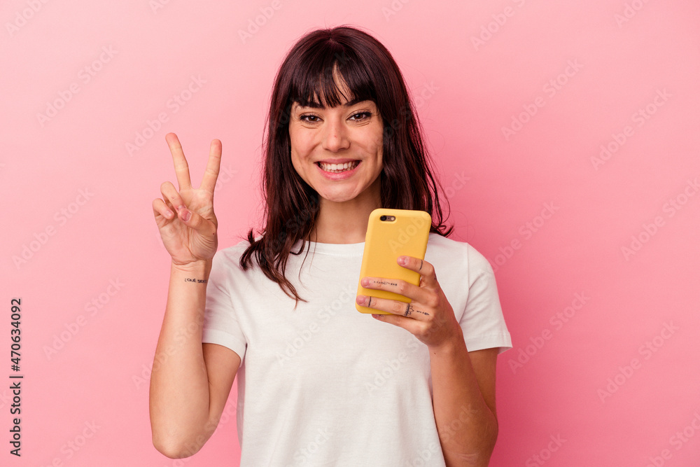 Young caucasian woman holding a mobile phone isolated on pink background showing number two with fingers. Young caucasian woman holding a mobile phone isolated on pink background showing number two with fingers.