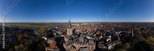 Tower town Zutphen in The Netherlands with medieval Hanseatic city center on the river IJssel and Walburgiskerk centrally in the frame. Aerial panorama of Dutch settlement against a clear blue sky.