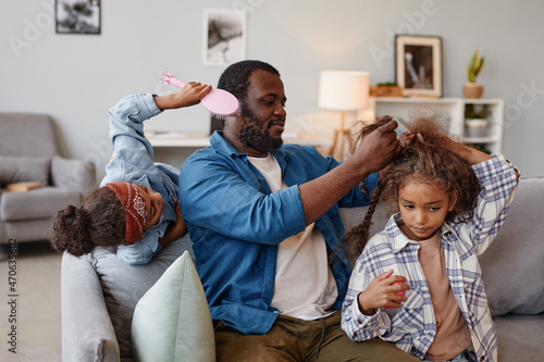 Portrait of African-American single father brushing hair of two cute girls at home, copy space