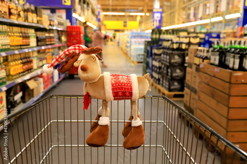 Funny Christmas deer on supermarket trolley. Shopping in the shop before the New Year, sale. A basket in wholesale store, background of blurred shelves with groceries and goods.