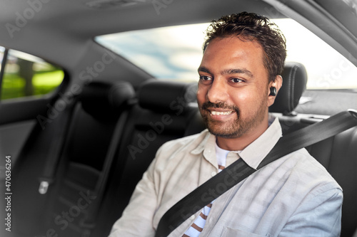 transportation, technology and people concept - happy smiling indian male passenger with wireless earphones on back seat of taxi car © Syda Productions