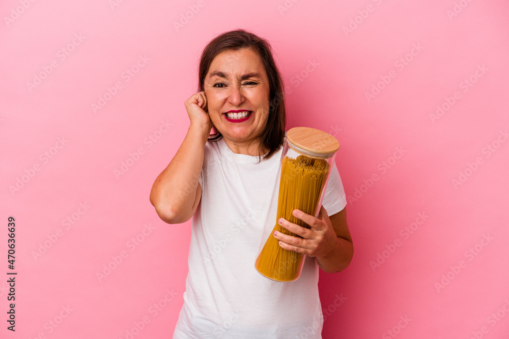 Middle age caucasian woman holding a pasta jar isolated on pink background covering ears with hands.