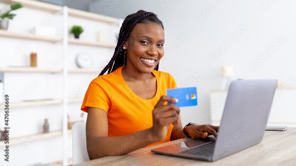 E-commerce. Millennial African American lady using credit card for remote payment, shopping online via laptop at home E-commerce. Millennial African American lady using credit card for remote payment, shopping online via laptop at home