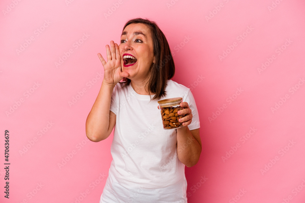 Middle age caucasian woman holding an almond jar isolated on pink background shouting and holding palm near opened mouth. Middle age caucasian woman holding an almond jar isolated on pink background shouting and holding palm near opened mouth.