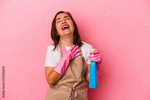 Middle age caucasian woman cleaning home isolated on pink background laughs out loudly keeping hand on chest.