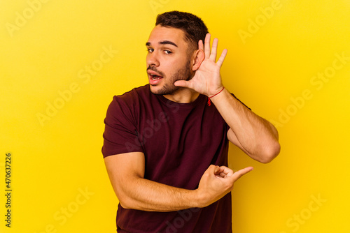 Young caucasian man isolated on yellow background trying to listening a gossip.