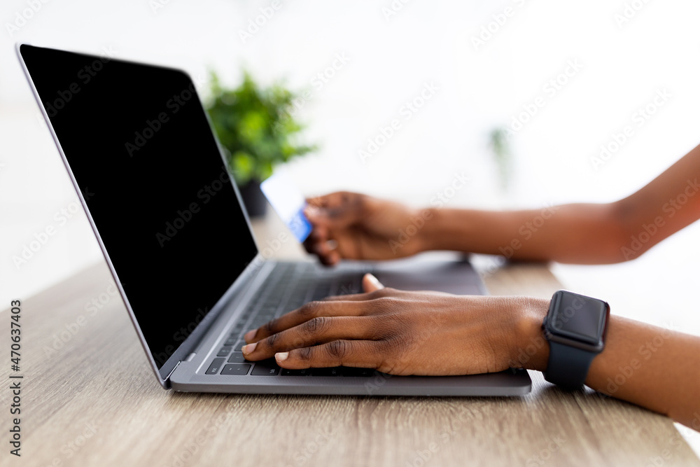 Naklejka premium Closeup of black lady using laptop and credit card to shop online from home, mockup for shopping website on screen