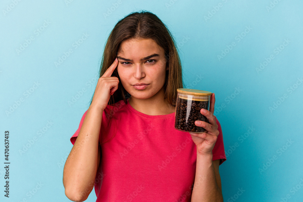 Young caucasian woman holding a coffee jar isolated on blue background pointing temple with finger, thinking, focused on a task. Young caucasian woman holding a coffee jar isolated on blue background pointing temple with finger, thinking, focused on a task.