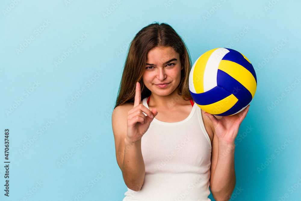 Young caucasian woman playing volleyball isolated on blue background showing number one with finger.