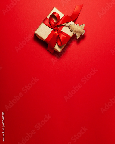 Brown paper gift box with a red satin ribbon bow and wooden tree on top on red background. Christmas holiday mother and father Valentines days and birthday present flat lay concept with copy space