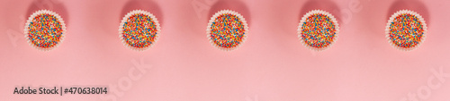 Banner of cupcake liners with colored sugar inside at the top from above. Flat lay top view. Confectionery cooking concept on bright pink paper background. National cooking day
