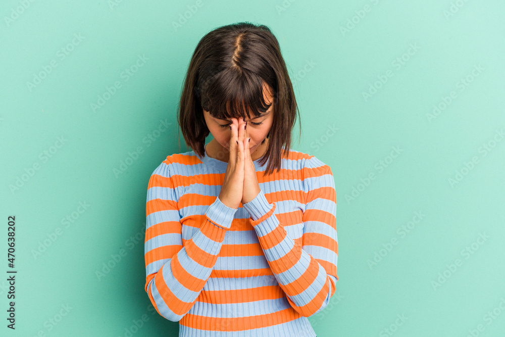 Young mixed race woman isolated on blue praying, showing devotion, religious person looking for divine inspiration. Young mixed race woman isolated on blue praying, showing devotion, religious person looking for divine inspiration.
