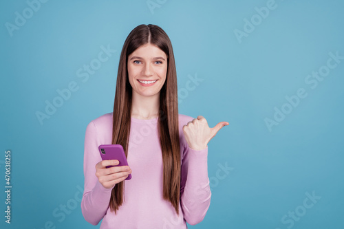Photo of excited cheerful girl point thumb empty space advert select promo cellphone isolated blue color background