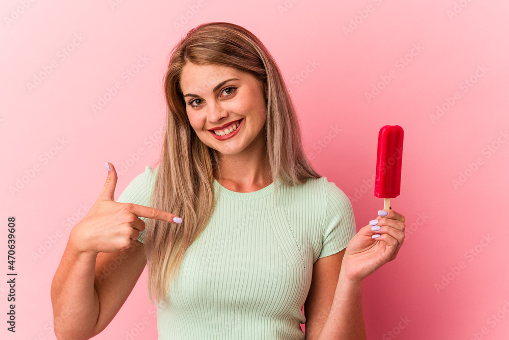 Young russian woman holding an ice cream isolated on pink background person pointing by hand to a shirt copy space, proud and confident Young russian woman holding an ice cream isolated on pink background person pointing by hand to a shirt copy space, proud and confident