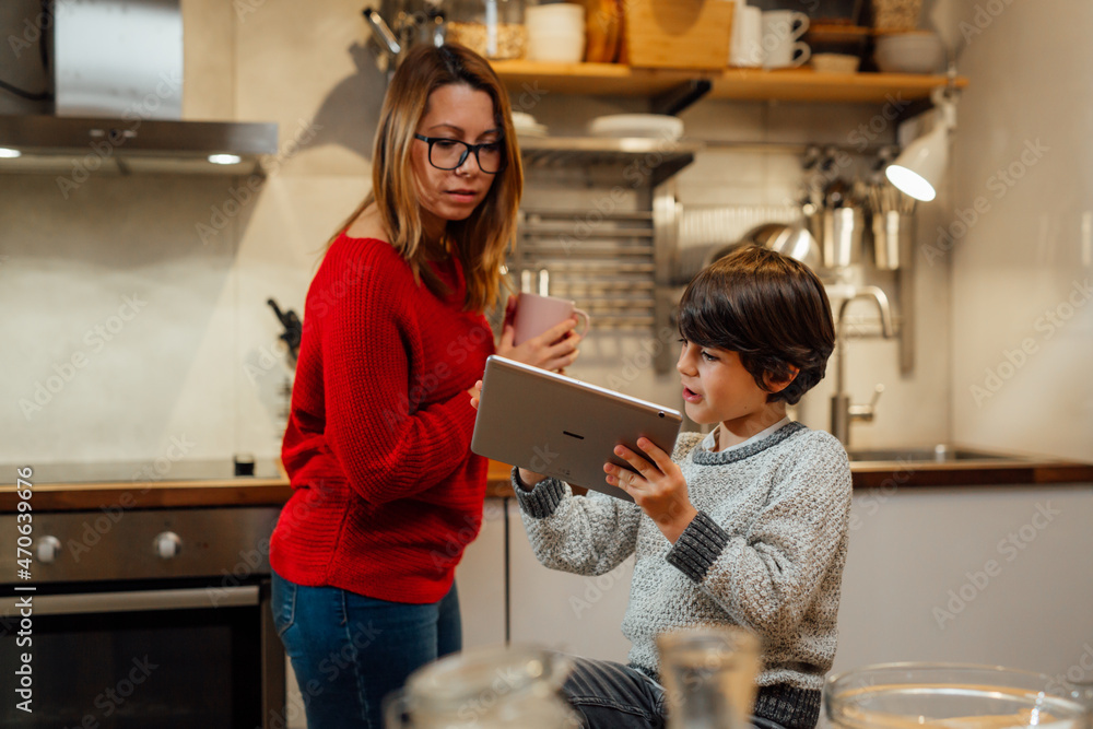 mother and her son looking recipes on digital tablet in kitchen mother and her son looking recipes on digital tablet in kitchen