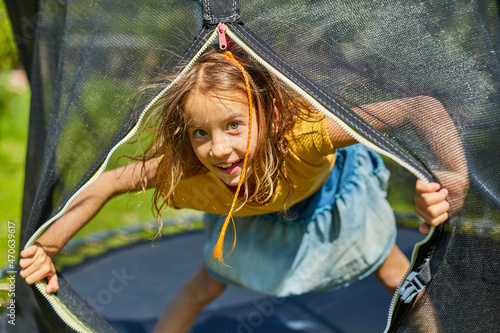 Portrait of young girl on her trampoline outdoors, in the backyard of the house on a sunny summer day, summertime vacation, Happy little child jumping on trampoline