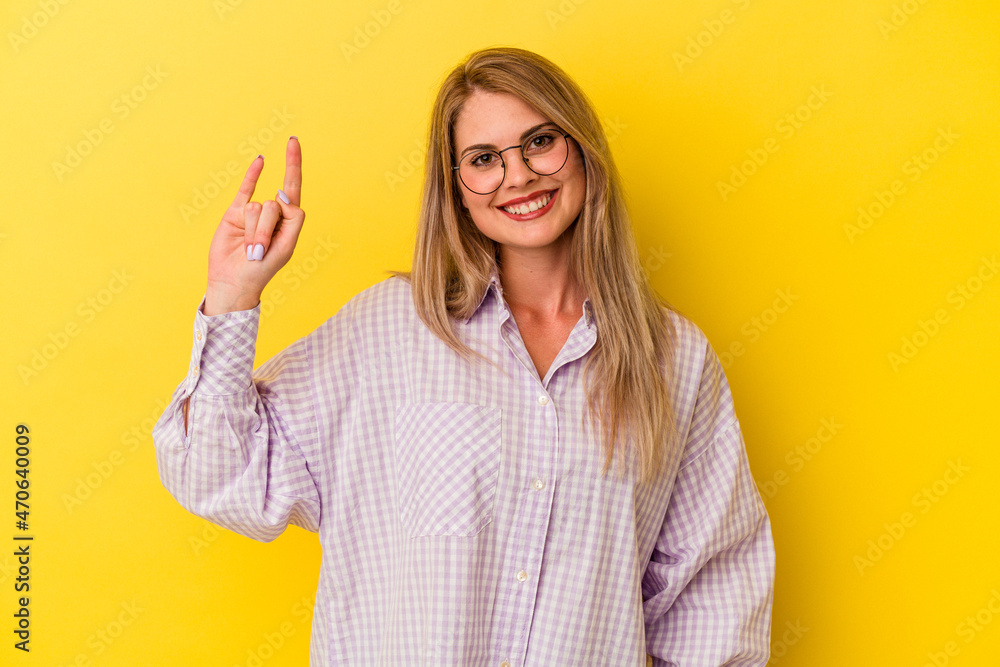 Young russian woman isolated on yellow background showing a horns gesture as a revolution concept. Young russian woman isolated on yellow background showing a horns gesture as a revolution concept.