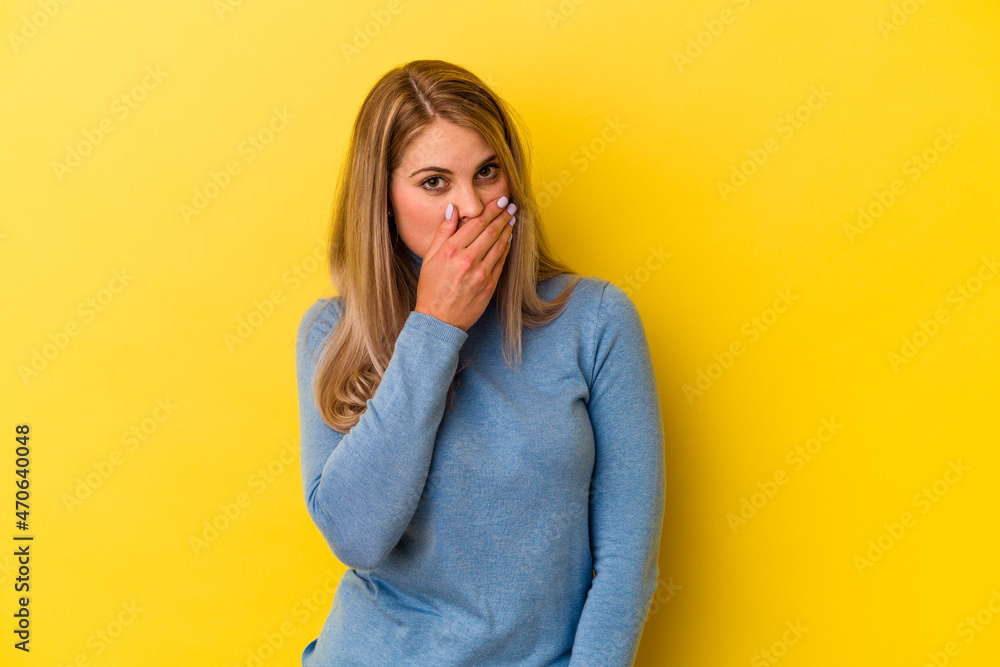Young russian woman isolated on yellow background covering mouth with hands looking worried. Young russian woman isolated on yellow background covering mouth with hands looking worried.
