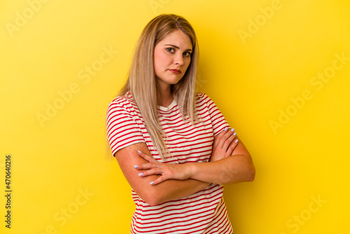 Young russian woman isolated on yellow background frowning face in displeasure, keeps arms folded.