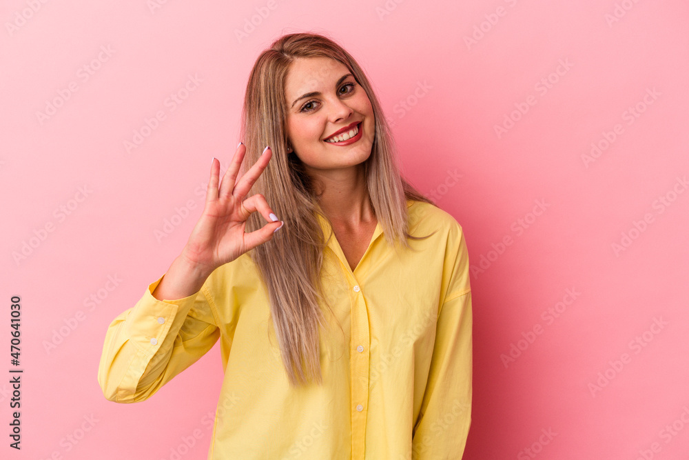 Fototapeta premium Young russian woman isolated on pink background winks an eye and holds an okay gesture with hand.