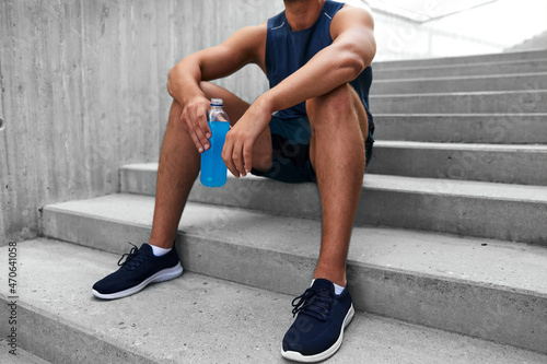 fitness, sport and people concept - tired young man with bottle of isotonic energy drink sitting on stairs