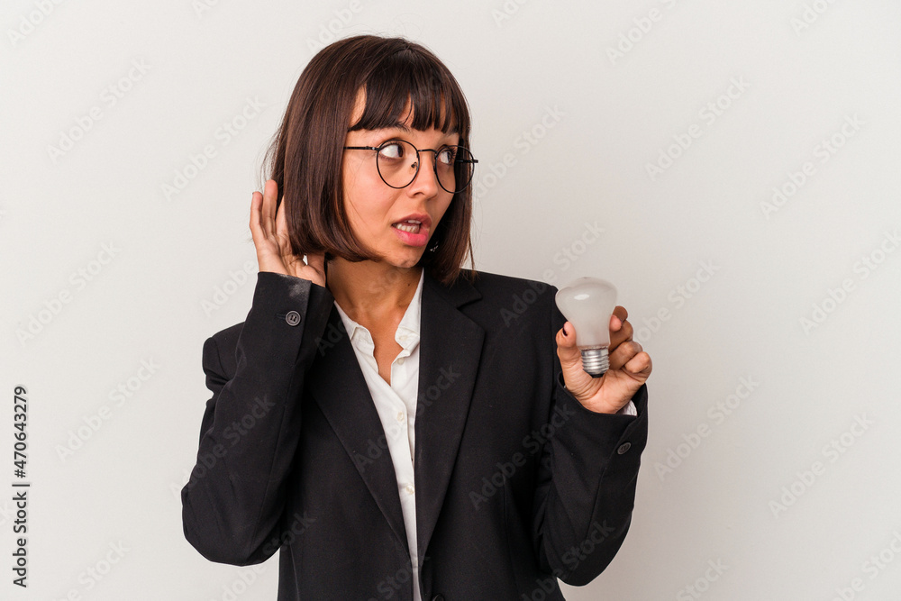 Young mixed race business woman holding a light bulb isolated on white background trying to listening a gossip. Young mixed race business woman holding a light bulb isolated on white background trying to listening a gossip.