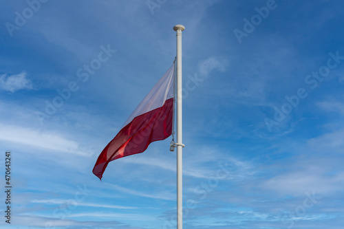 The national flag of Poland flies against a blue sky and a few white clouds.
