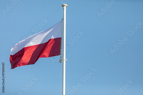 The flag of Poland flying in the wind on a tall pole against a blue sky.