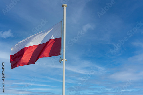 The national flag of Poland flies against a blue sky and a few white clouds.