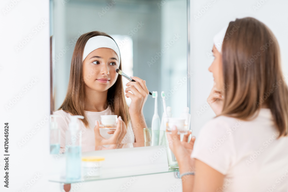 beauty, make up and cosmetics concept - teenage girl with brush applying face mask and looking to mirror at home bathroom beauty, make up and cosmetics concept - teenage girl with brush applying face mask and looking to mirror at home bathroom