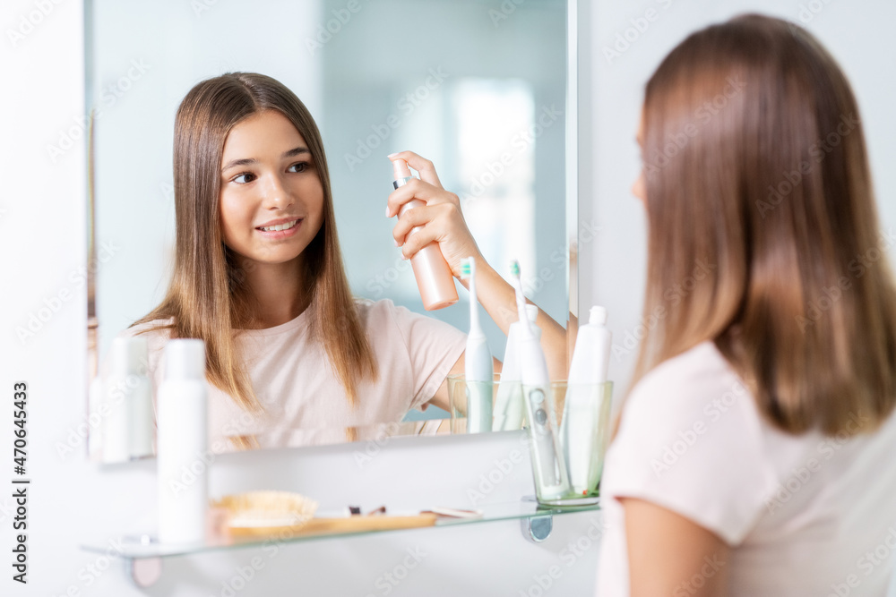 beauty and people concept - teenage girl looking to mirror and using hair styling spray at home bathroom beauty and people concept - teenage girl looking to mirror and using hair styling spray at home bathroom