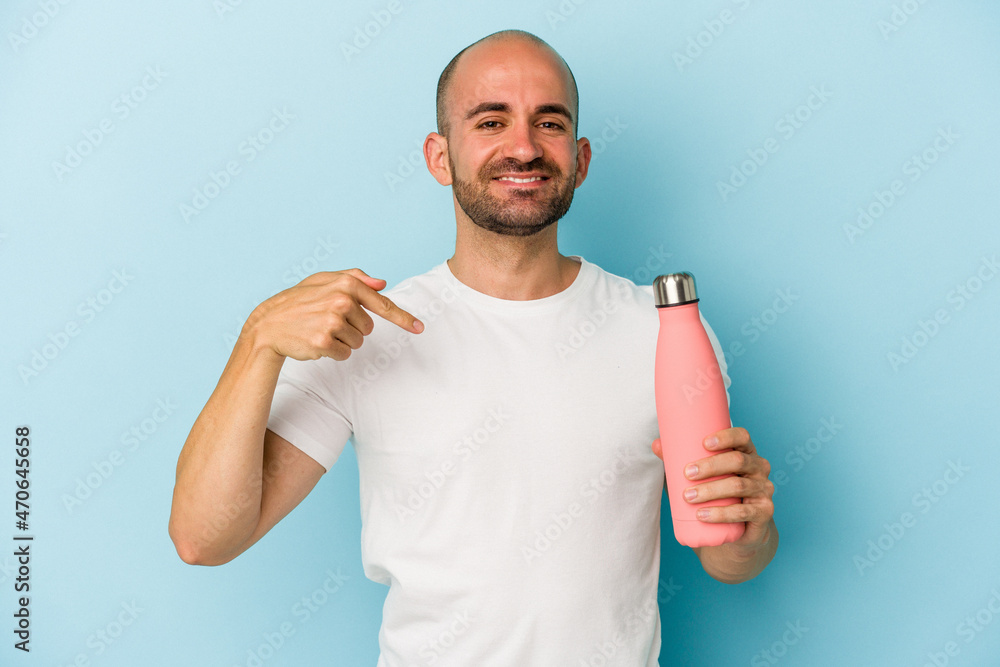 Young bald man holding canteen isolated on blue background person pointing by hand to a shirt copy space, proud and confident Young bald man holding canteen isolated on blue background person pointing by hand to a shirt copy space, proud and confident