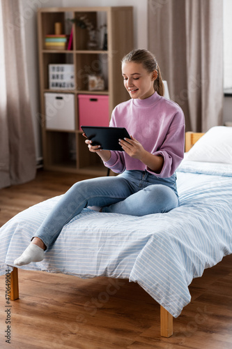 children, technology and communication concept - smiling teenage girl with tablet computer sitting on bed at home