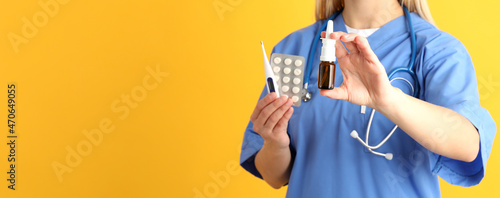Young nurse with nasal spray on yellow background, seasonal cold treatment