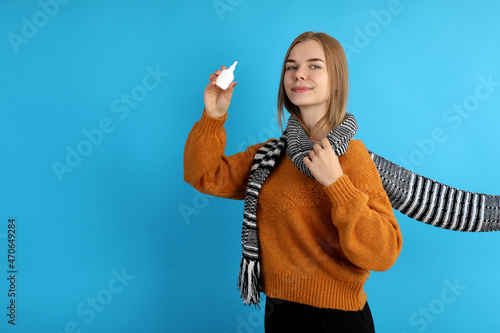 Young woman with nasal drops on blue background, runny nose concept photo