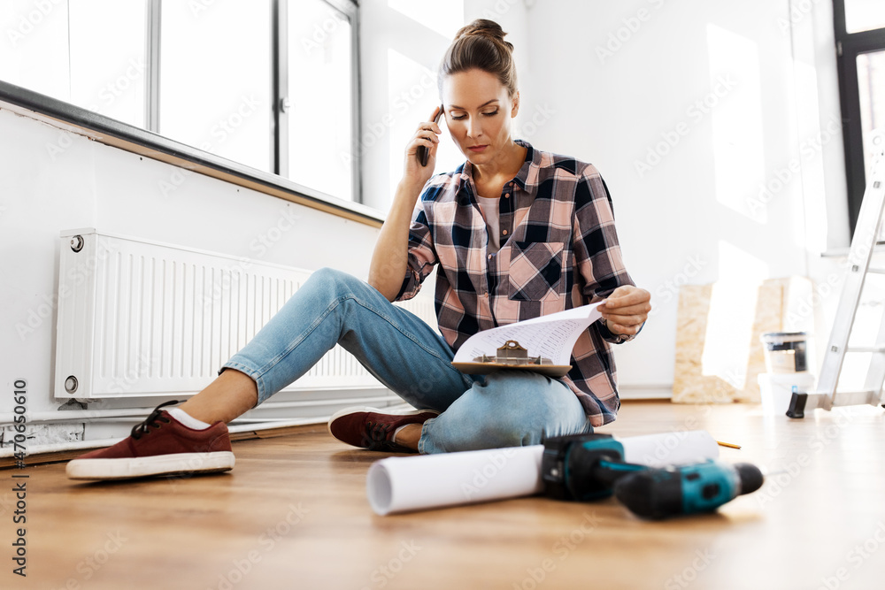 repair, people and real estate concept - woman with clipboard calling on smartphone sitting on floor at home