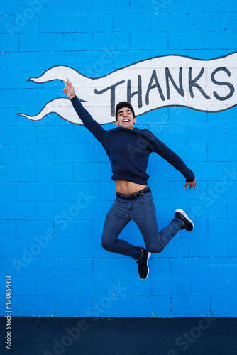 Fototapeta Naklejka Na Ścianę i Meble -  Portrait of the young man jumping against blue background with word thanks on it
