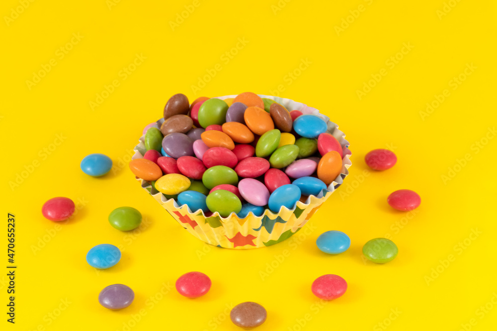 Colorful chocolate candy pills in bowl on yellow background